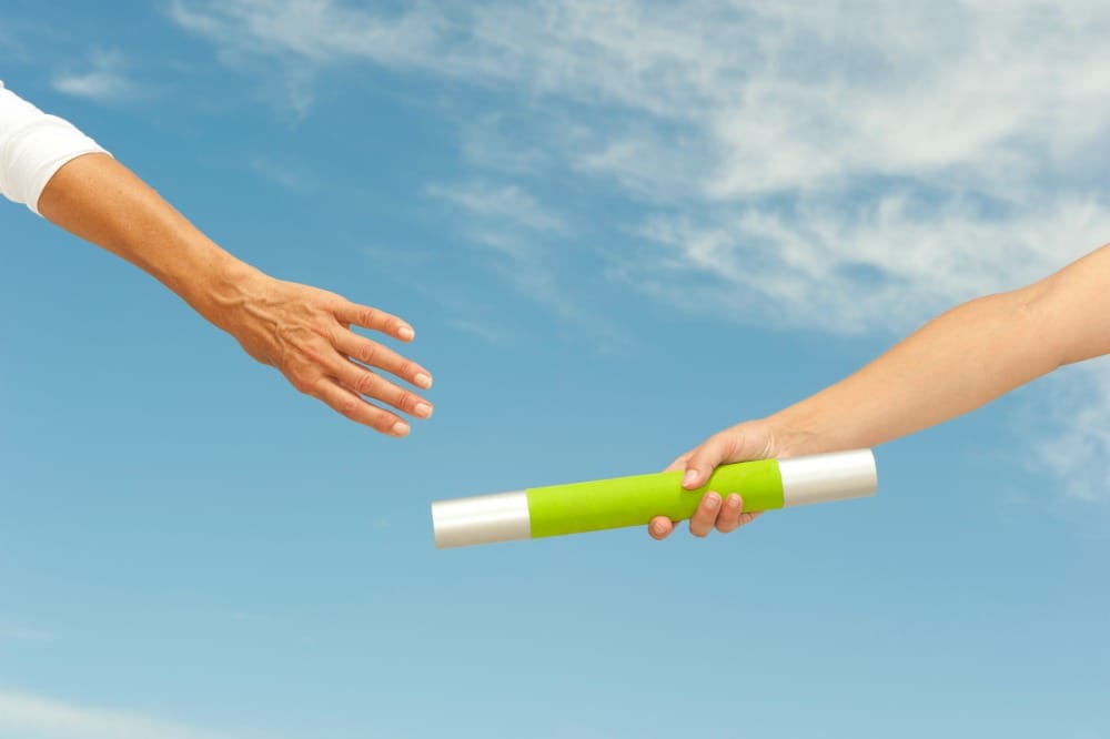 Hands of track and field athletes with relay baton, symbol for teamwork, partnership, cooperation, isolated with blue sky as background and copy space.
